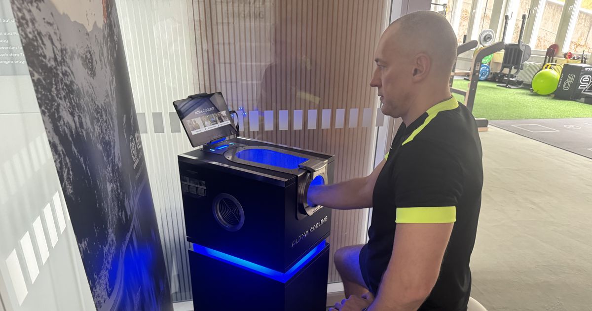 Person im ONE/1-Shirt sitzt im Lab in Baierbrunn am Alpha-Cooling-Gerät, eine Hand liegt in der blau beleuchteten Kühlöffnung, daneben das Display des Geräts