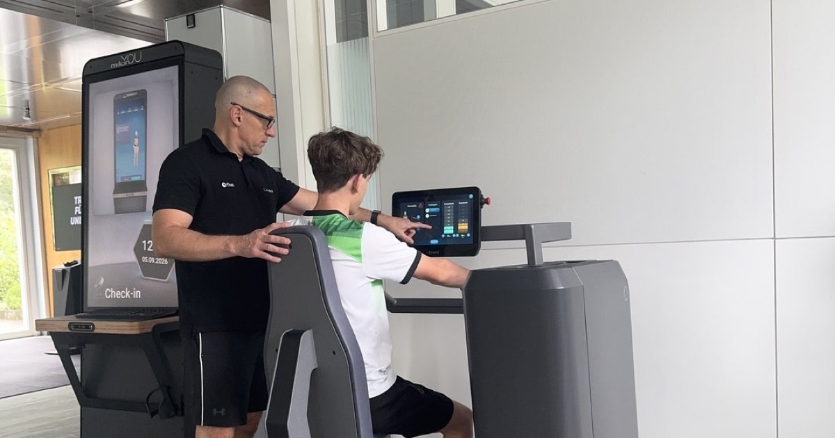 Marius Seifert weist im ONE/1 Lab in Baierbrunn einen Trainierenden an einem milon-Gerät ein, das Display am Gerät zeigt die Werte