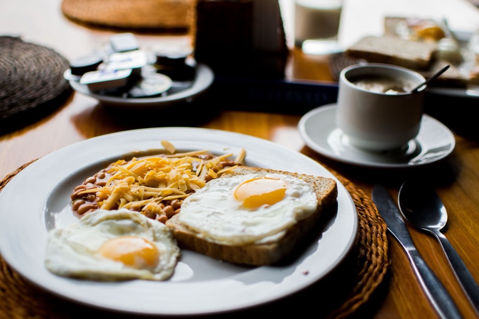Frühstücksteller mit zwei Spiegeleiern, Toast und Bohnen, daneben eine Tasse Kaffee