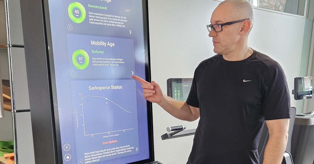 Mann am milon-Terminal im ONE/1 Lab, der Bildschirm zeigt Muscle Age, Mobility Age und Sarkopenie-Status