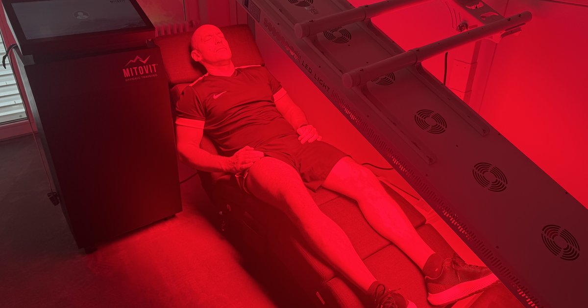 Marius Seifert liegt unter dem Rotlicht-Panel im ONE/1 Lab in Baierbrunn, der Raum ist rot ausgeleuchtet