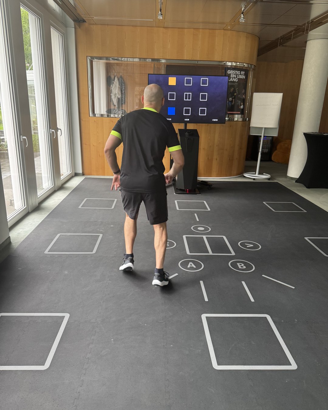 SKILLCOURT im ONE/1 in Baierbrunn: Marius Seifert läuft auf der markierten Matte ein aufleuchtendes Feld an, der Bildschirm zeigt das 3x3-Raster